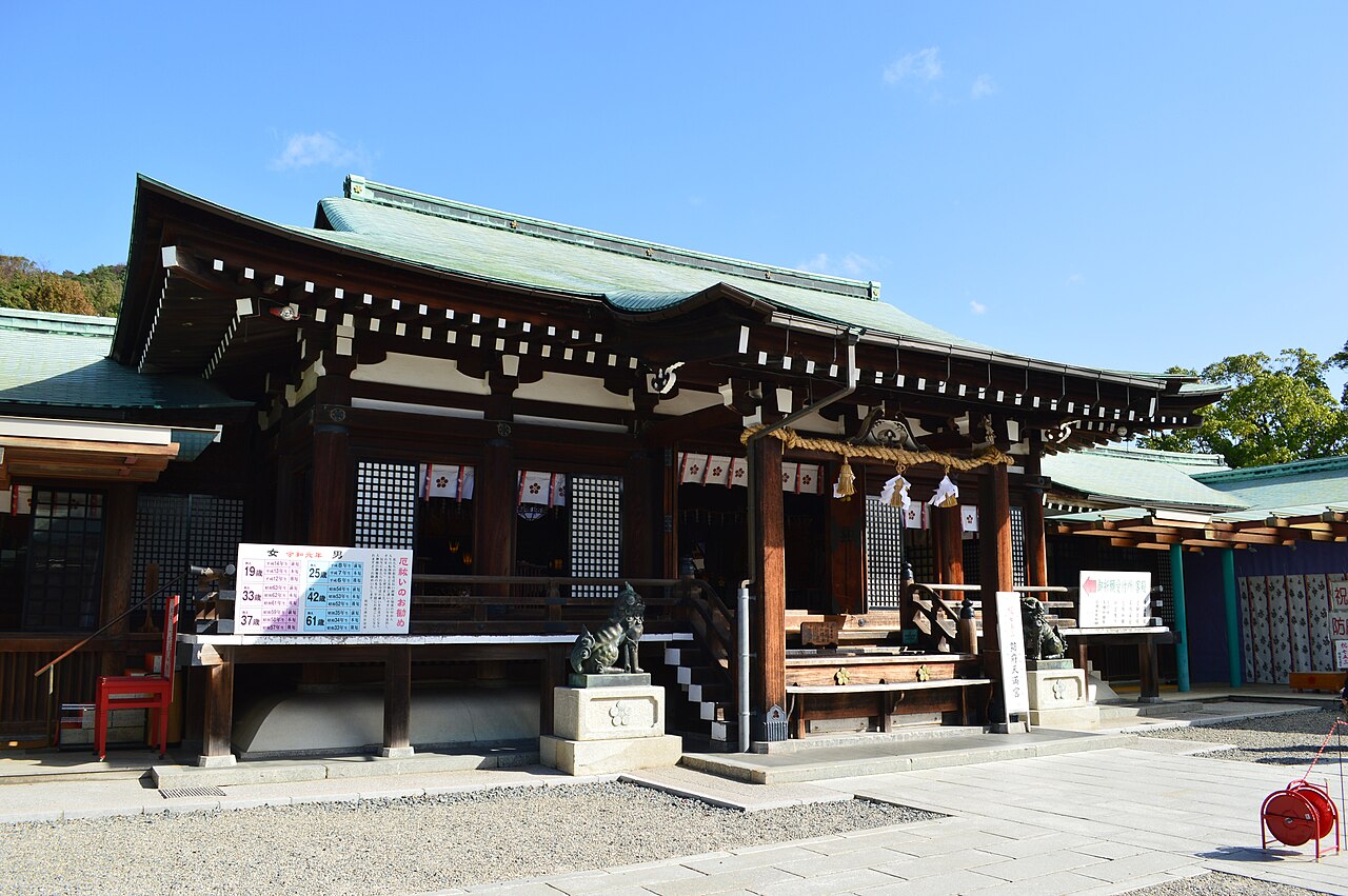 The worship hall of Hofu Tenmangu with a green copper roof, a thick sacred straw rope and stone guardian lions in front