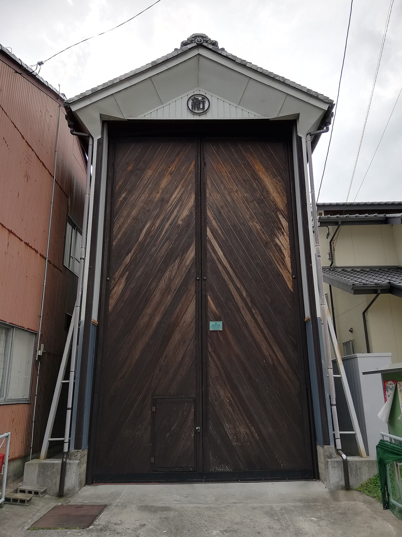A tall wooden storage building for an Inuyama Festival float, its weathered diagonal-plank doors closed beneath a tiled gable.