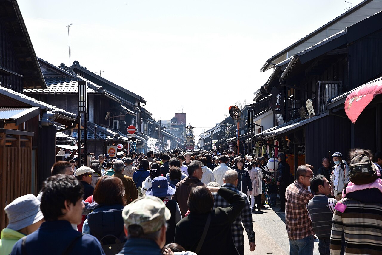A crowded street lined with dark wooden merchant houses in Inuyama's old castle town, with a festival float visible far down the lane.