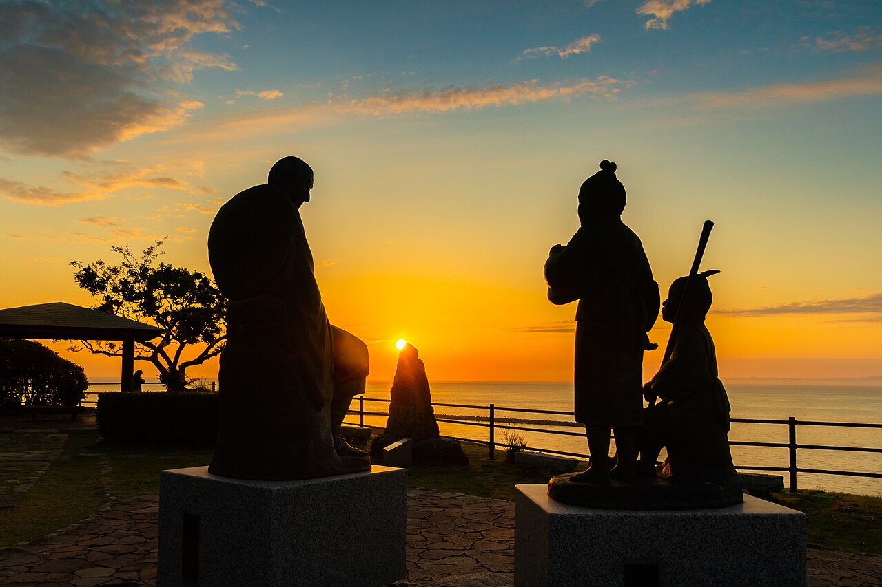 Statues of the monk Ryokan and children silhouetted against a sunset over the Sea of Japan at Ryokan and Yuhi-no-oka Park, Izumozaki.