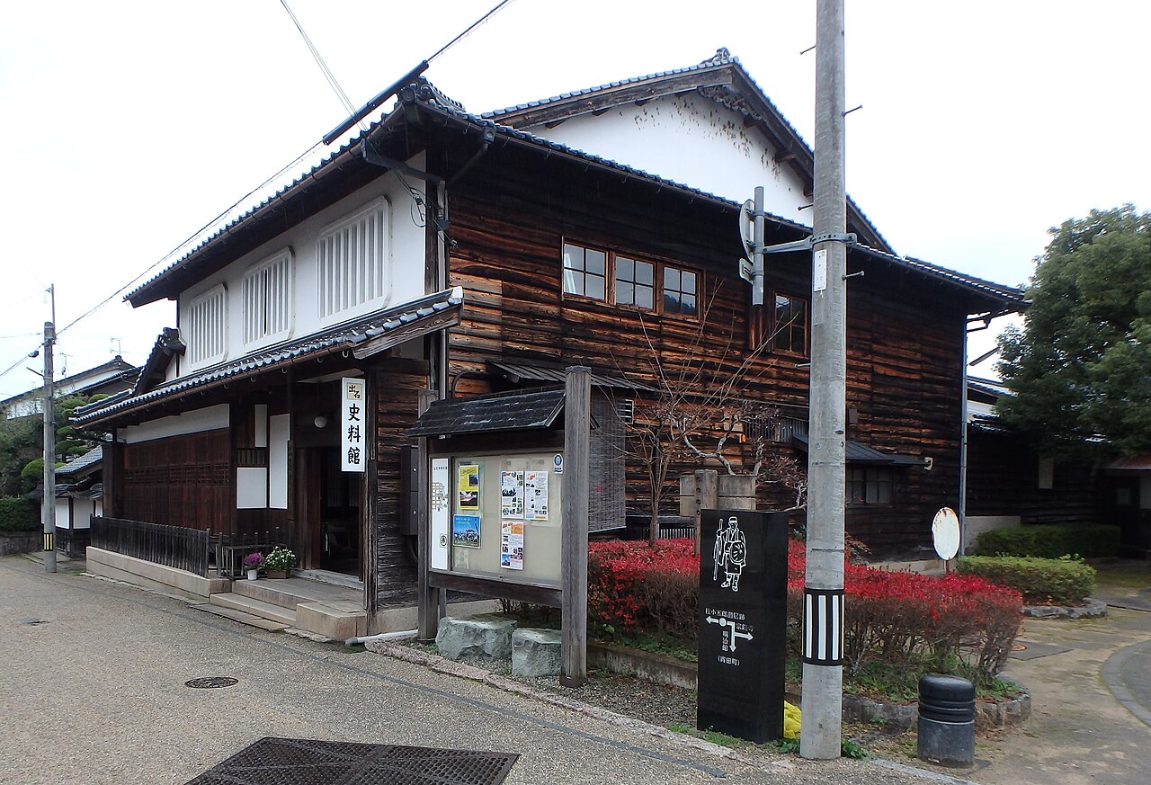 The two-storey former Fukutomi residence, now the Izushi history museum, with glass-fronted upper windows above a small garden of clipped shrubs turning red