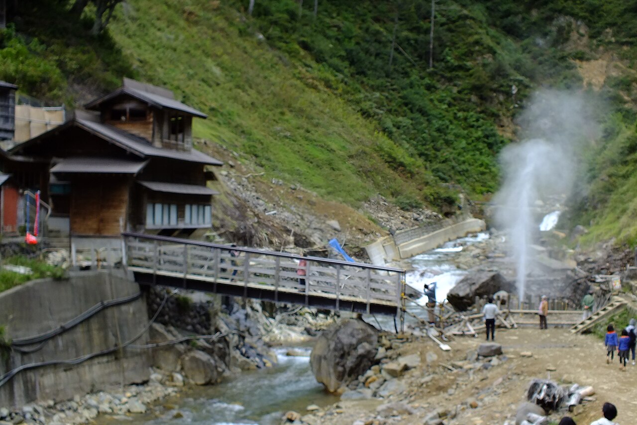 A column of hot water shoots up beside a footbridge in the valley.