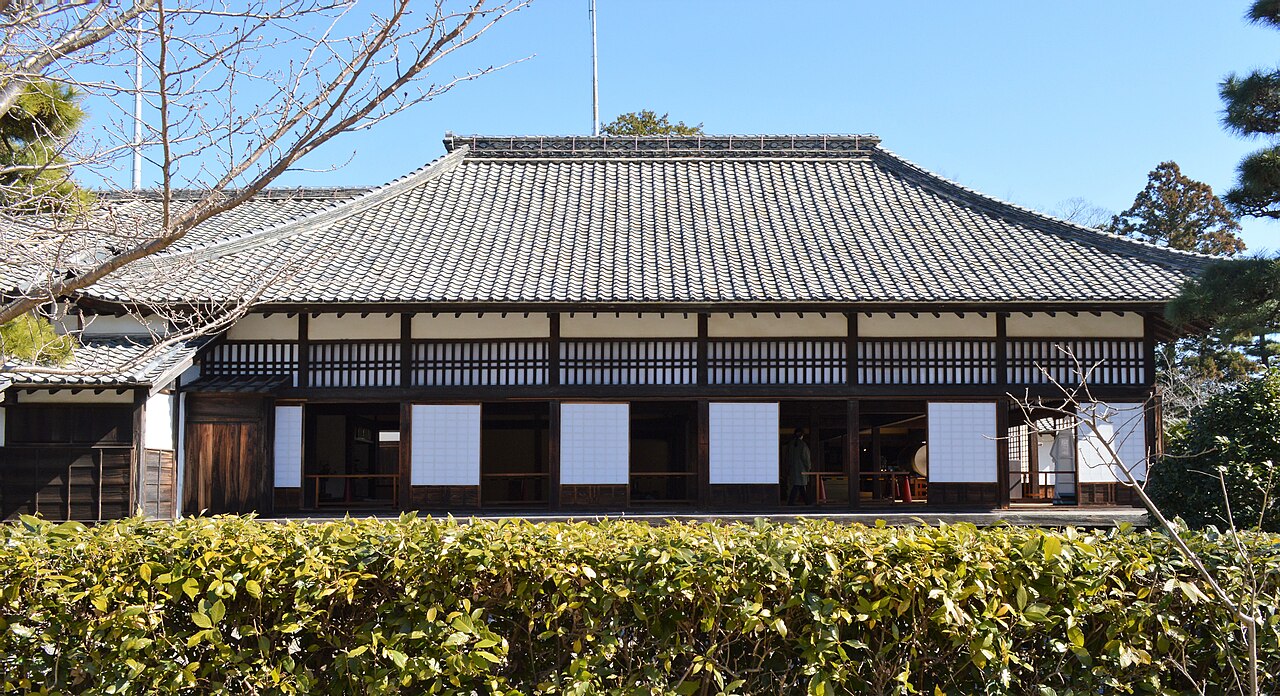 The long tiled roof and wooden front of Kakegawa Castle's Goten palace seen over a trimmed hedge