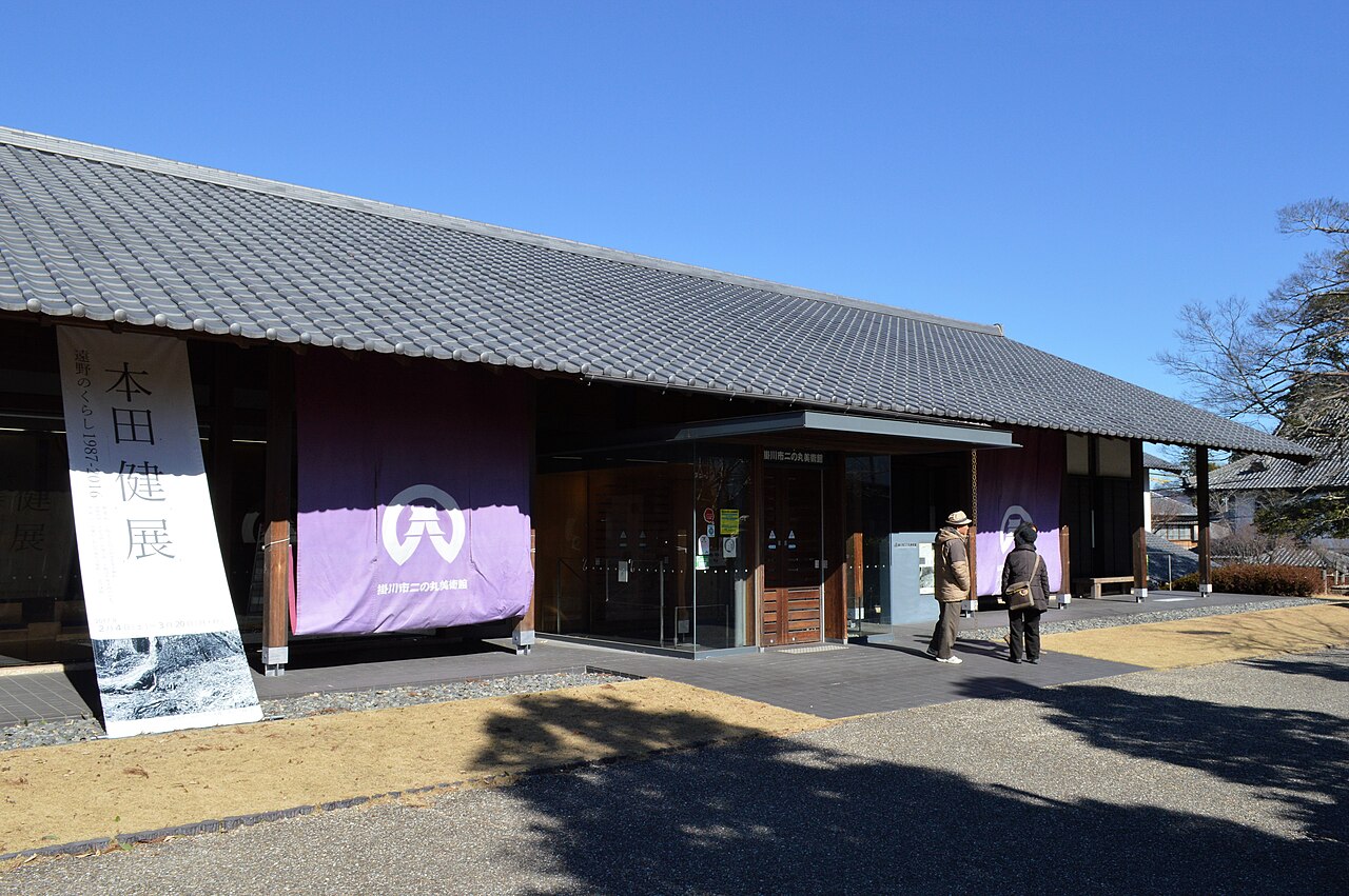 The low tiled-roof entrance of the Ninomaru Museum of Art with purple banners under a blue sky
