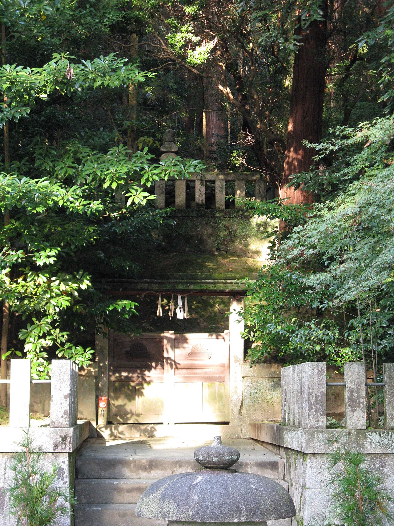 The Kusunoki Masashige head mound at Kanshinji, a stone-fenced enclosure behind a stone lantern among trees
