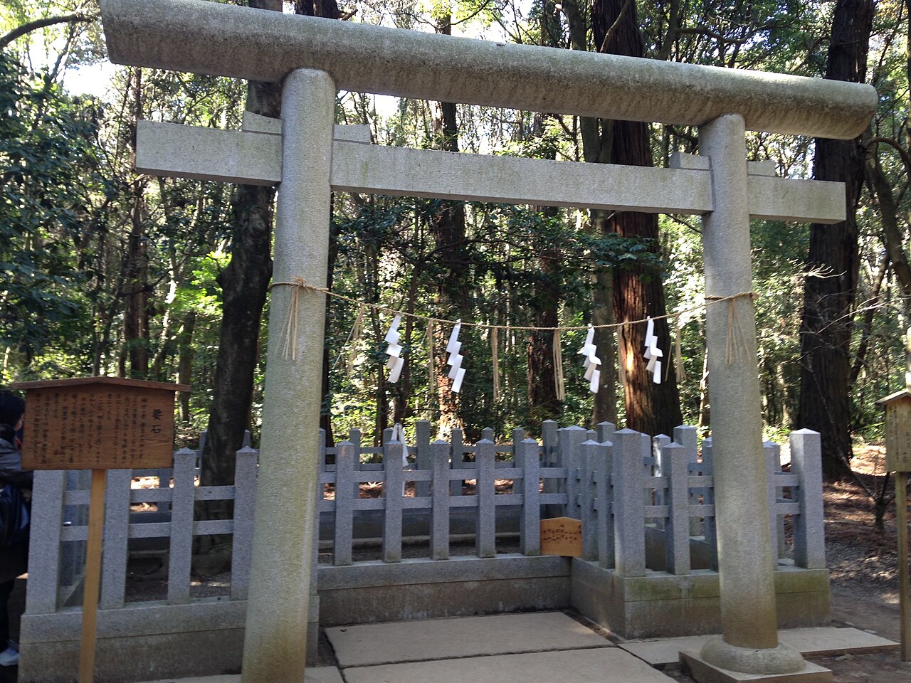 A stone torii and fence marking the Kaname-ishi keystone in the woods of Kashima Jingu