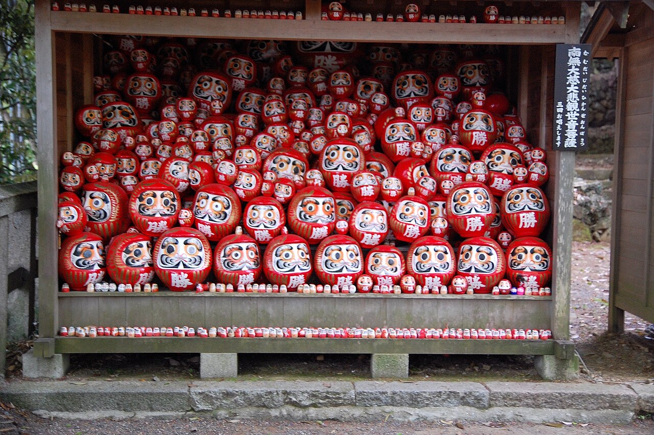 A wooden shelter packed with rows of red Daruma dolls offered at Katsuo-ji