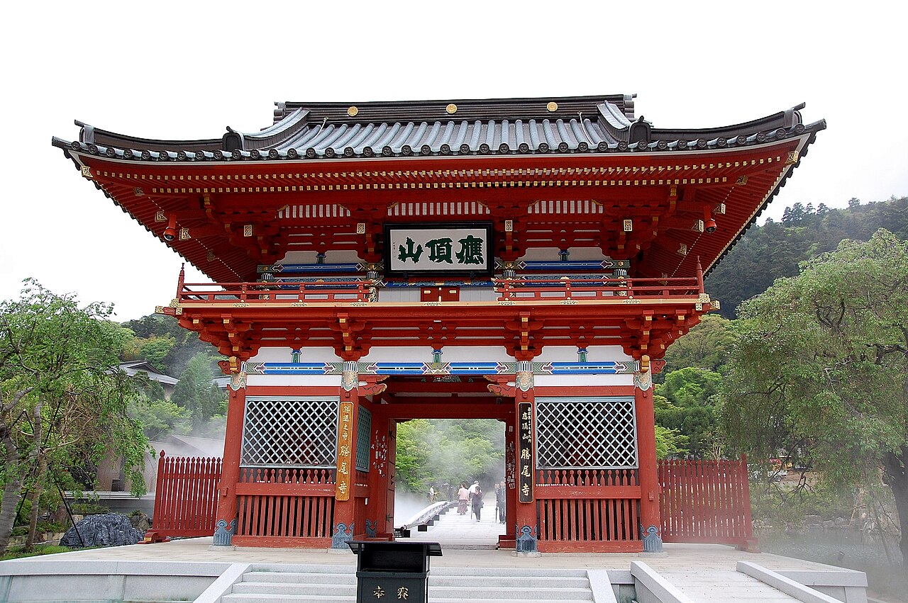 The two-storied red Sanmon gate of Katsuo-ji seen from the front, with green trees on both sides
