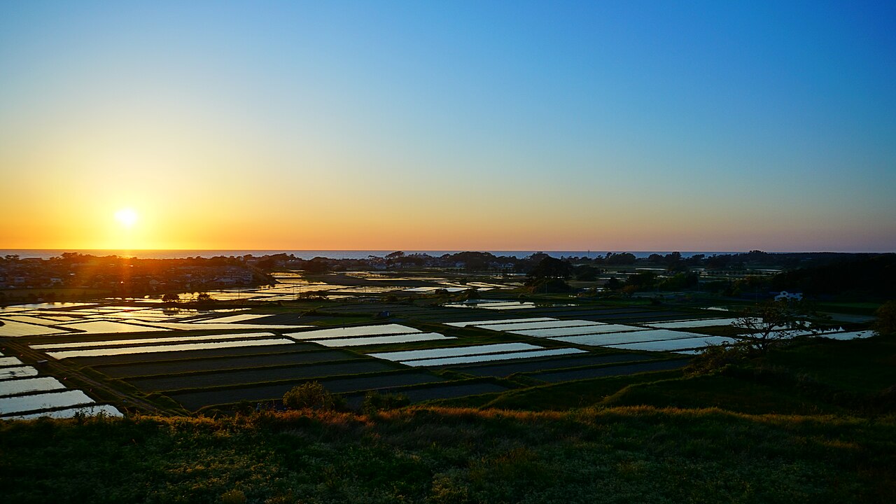 Flooded paddies at Kisakata reflecting the orange sky as the sun sets over the Sea of Japan on the horizon.