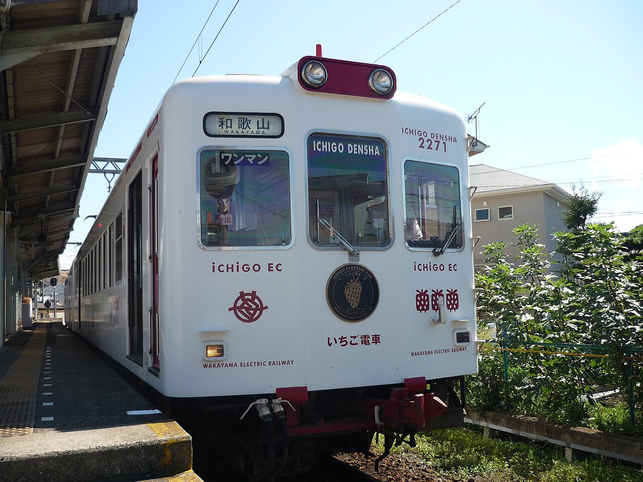 The white and red Ichigo Densha strawberry train of the Kishigawa Line standing at a platform, its front marked with a strawberry emblem and the destination Wakayama-Kishi