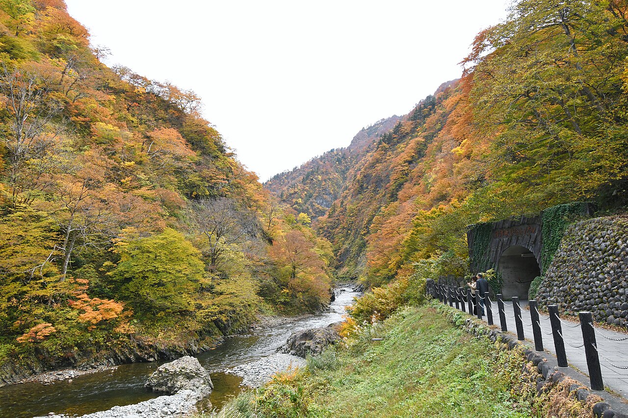 Autumn colour on both slopes of the gorge above the rocky Kiyotsu River, with a guard-railed road on the right.
