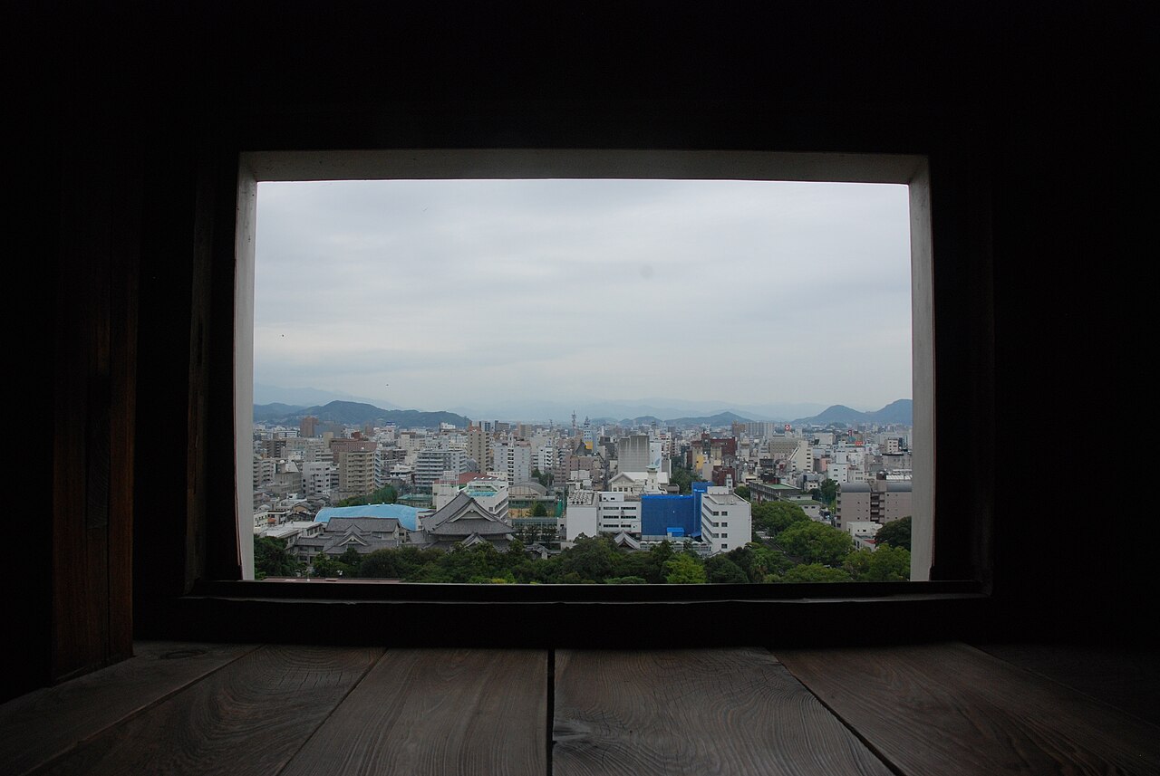 The city of Kochi and distant hills seen through a dark wooden window opening inside the castle keep.