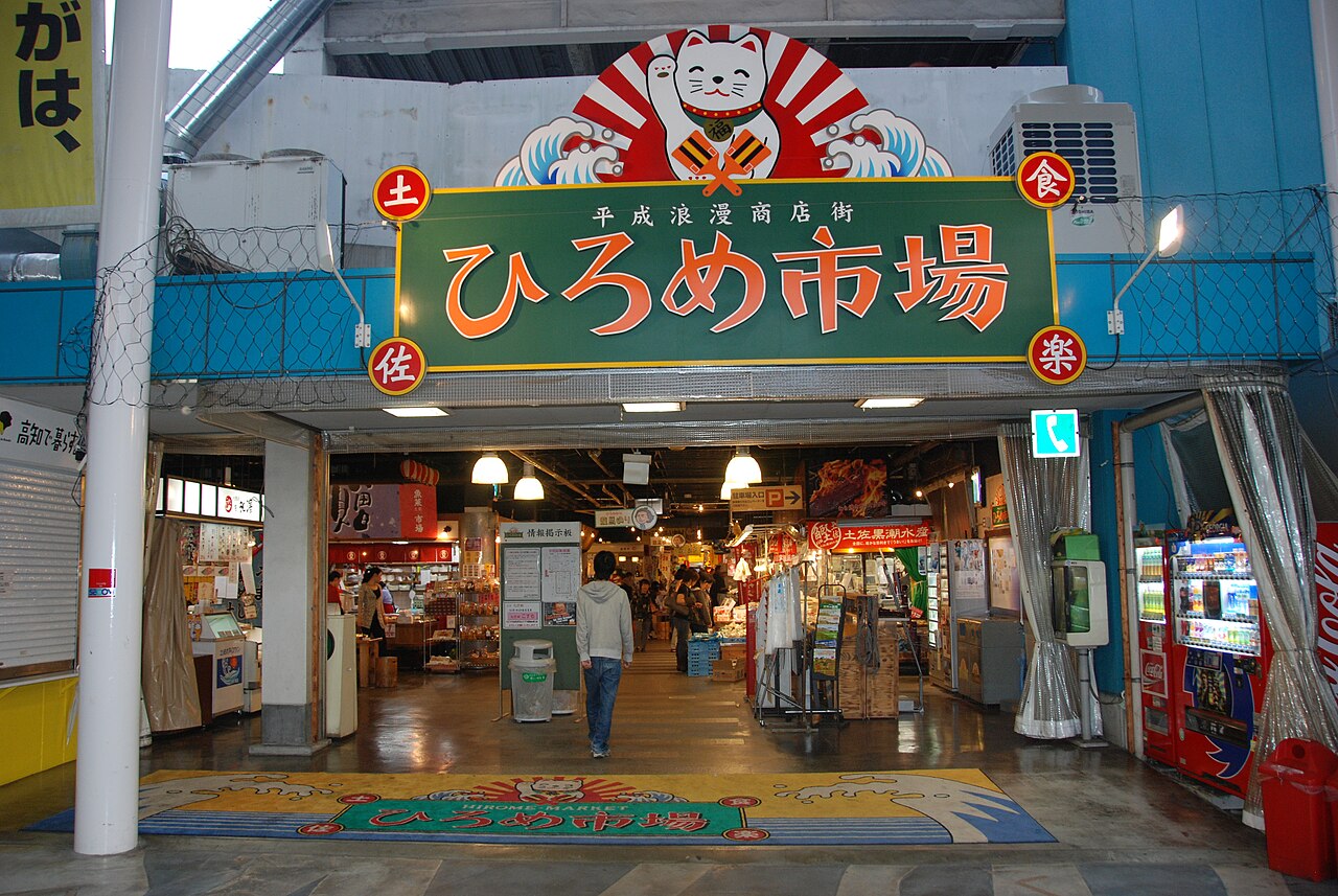 The entrance sign of Hirome Market in Kochi, with a lantern-lit arcade of small food stalls beyond.