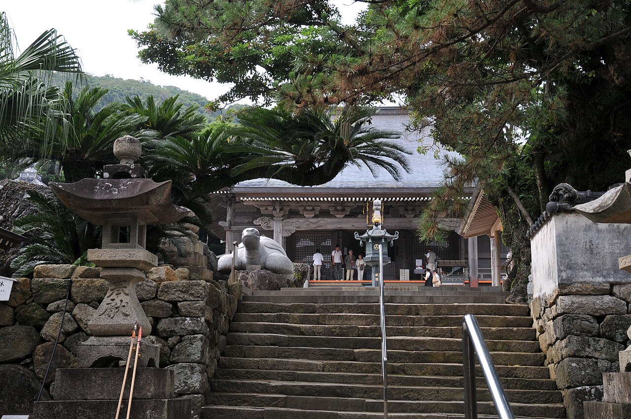 Stone steps leading up to the main hall of Kongofuku-ji temple, framed by palm and cycad trees