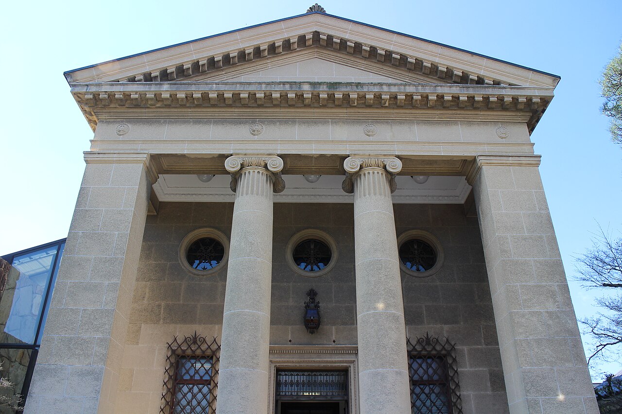 A neoclassical stone facade with a triangular pediment and four tall columns under a blue sky.