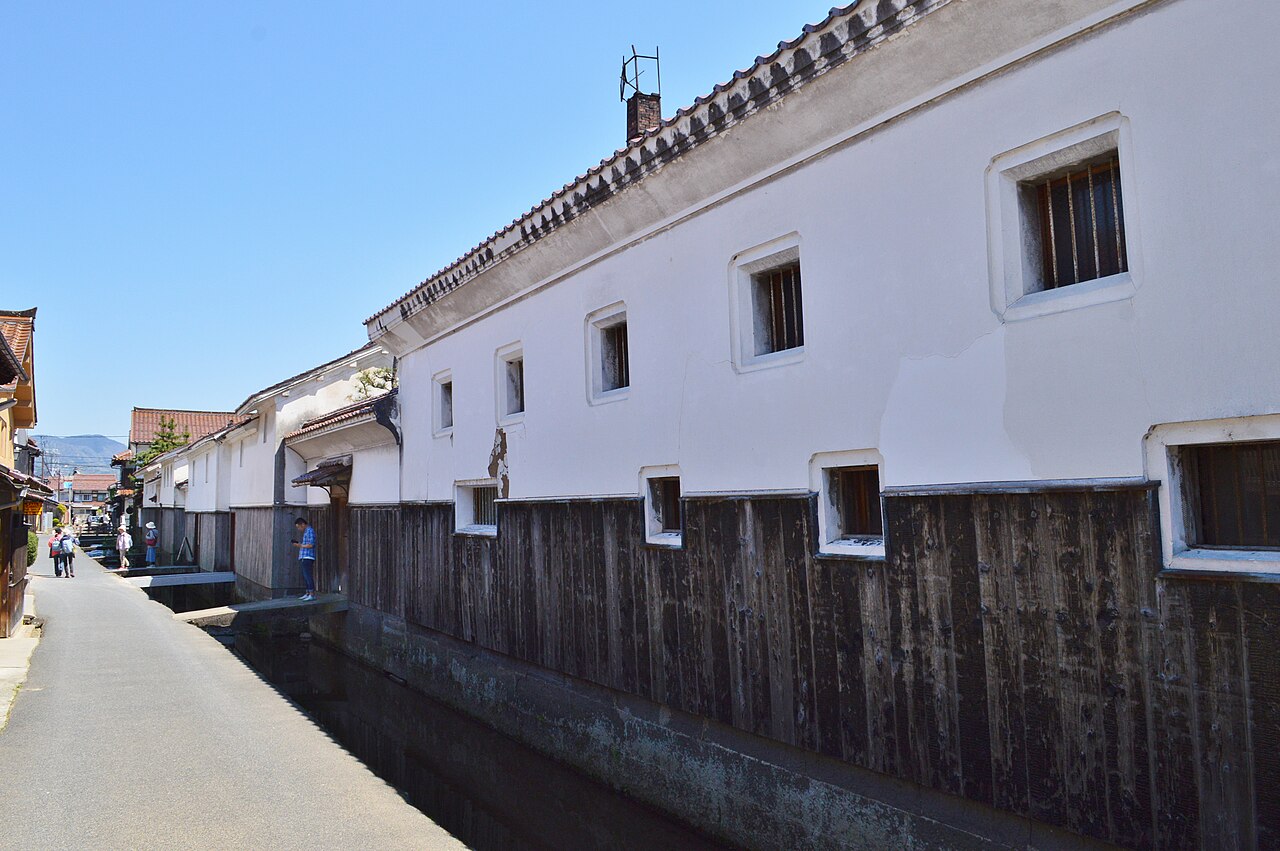 White-plastered storehouses with dark wooden lower walls along a narrow canal in Kurayoshi under a clear blue sky