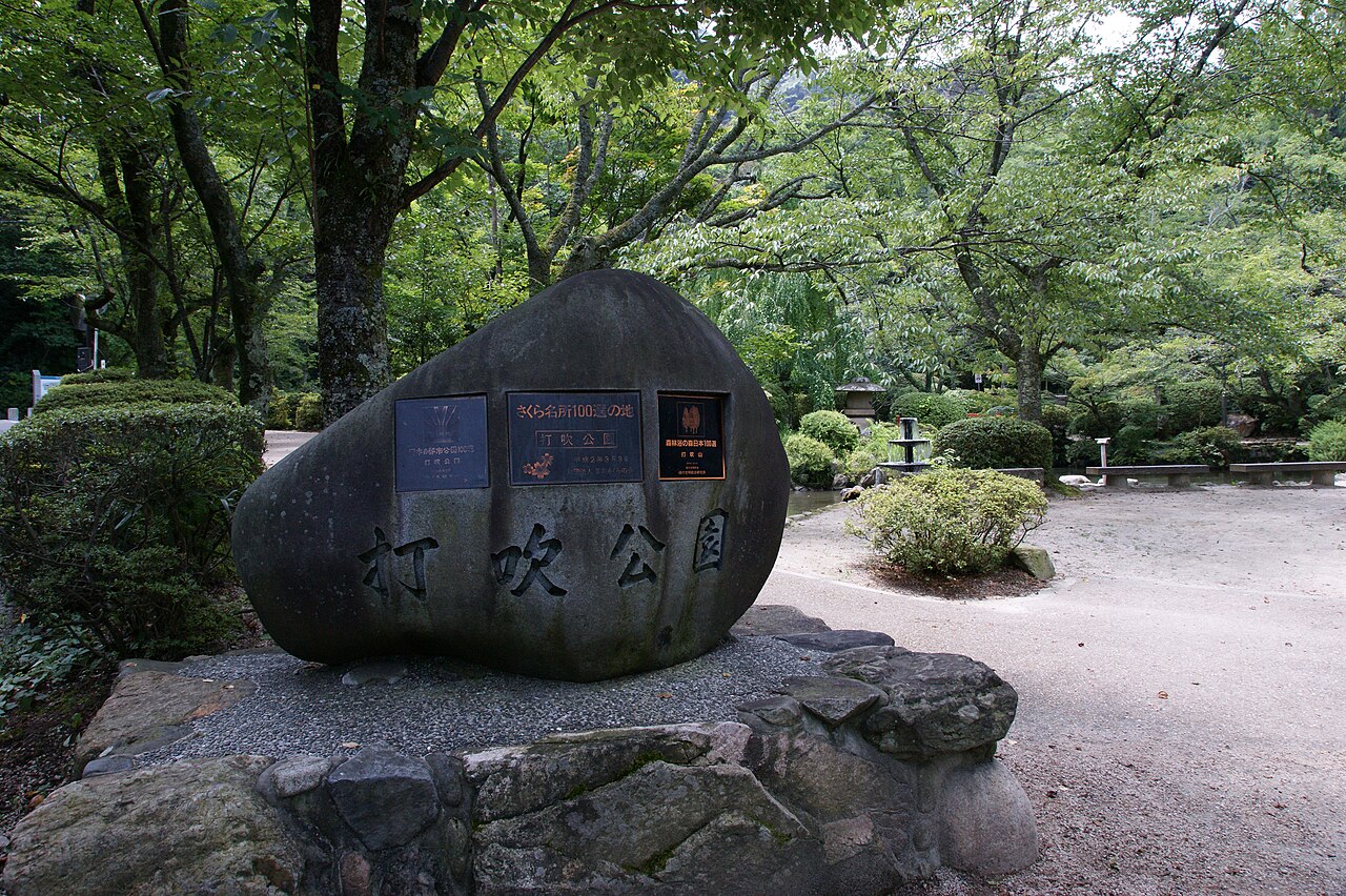 A stone marker for Utsubuki Park beside a path among green trees