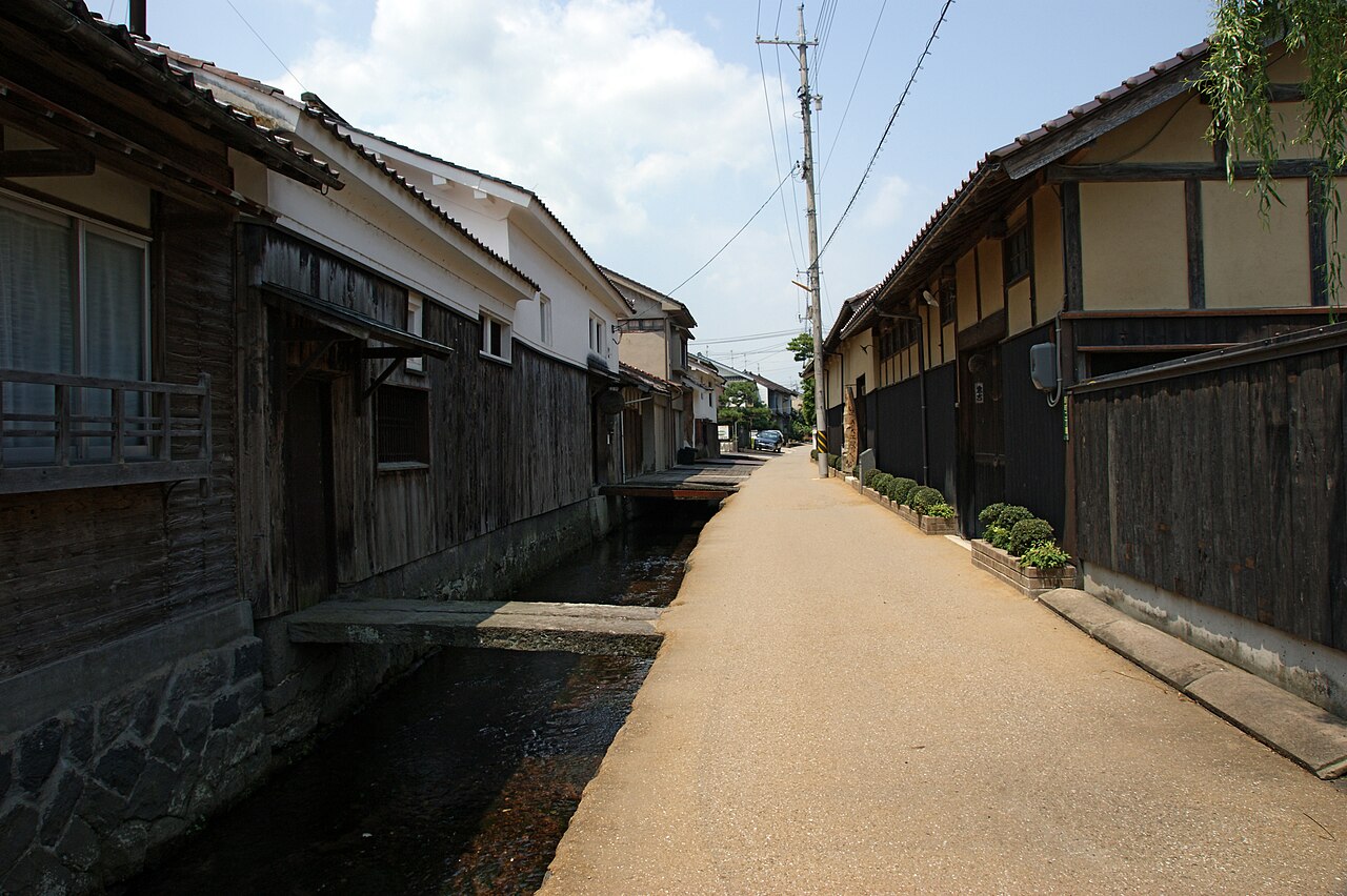 The Tamagawa canal with a small stone-slab bridge and old wooden houses along a narrow lane