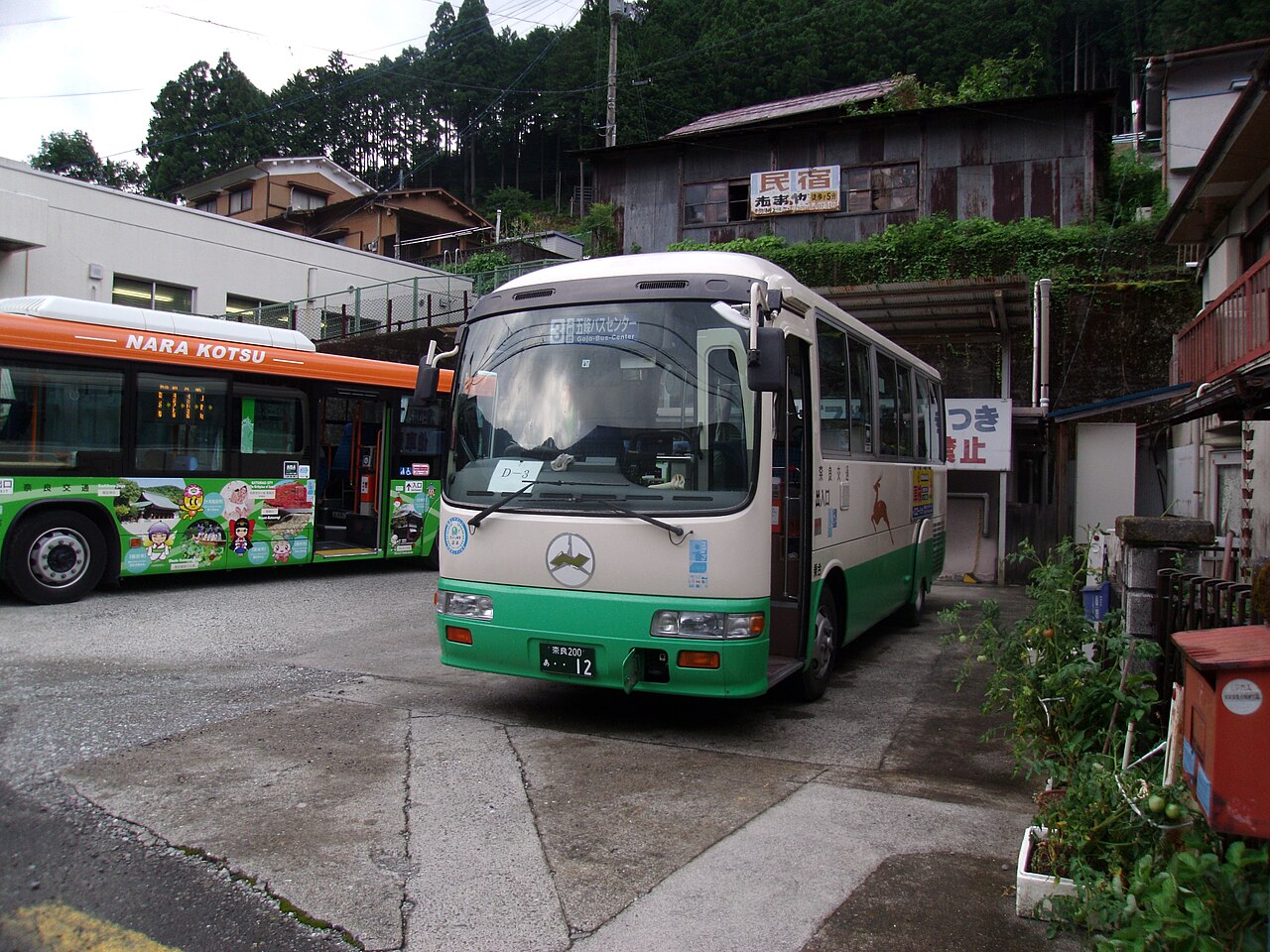 Two Nara Kotsu buses parked at a small bus station among wooded hills