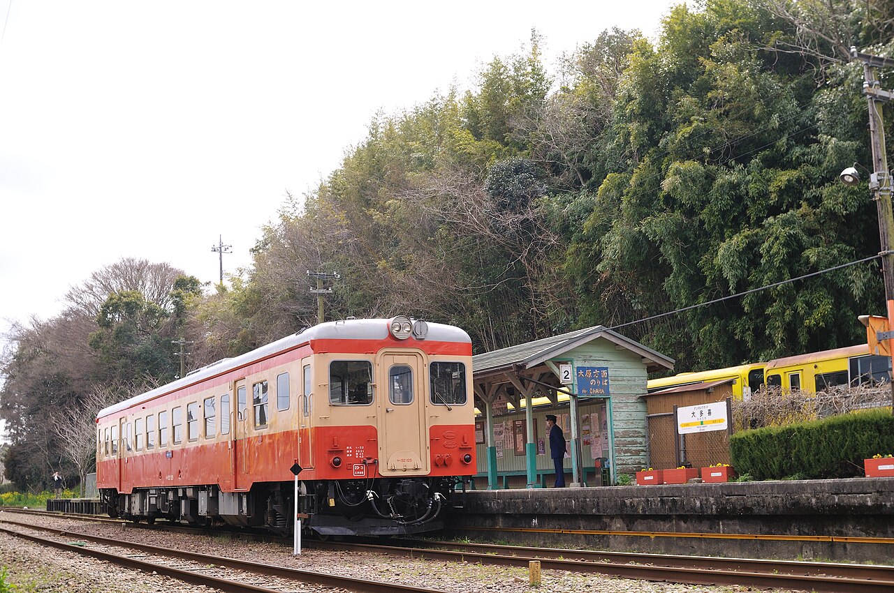 A vintage cream-and-orange Kiha 52 railcar waiting at Otaki Station on the Isumi Railway, with a station attendant on the platform.