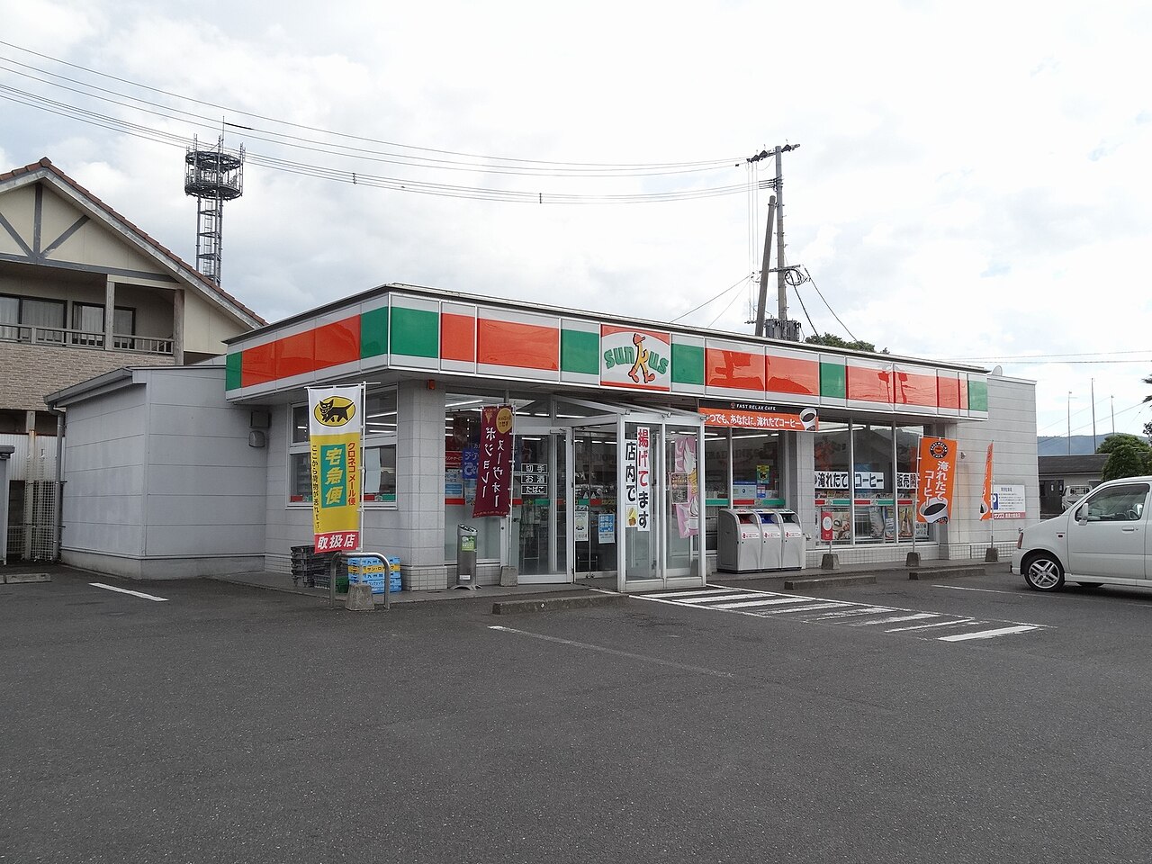A Sunkus convenience store with a yellow Kuroneko Yamato TA-Q-BIN handling-store banner standing in front of the entrance
