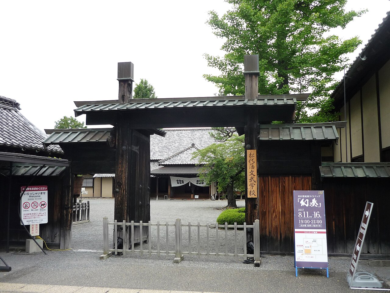 The wooden front gate of the old Bunbu Gakko domain school in Matsushiro, with a dark timber frame, tiled roofs and a signboard beside the entrance.