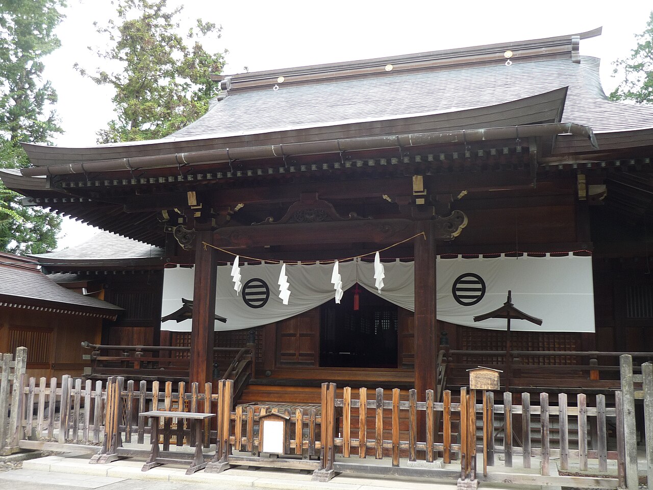 The wooden worship hall of Zozan Shrine in Matsushiro, hung with white curtains bearing a crest and fronted by a low wooden fence.