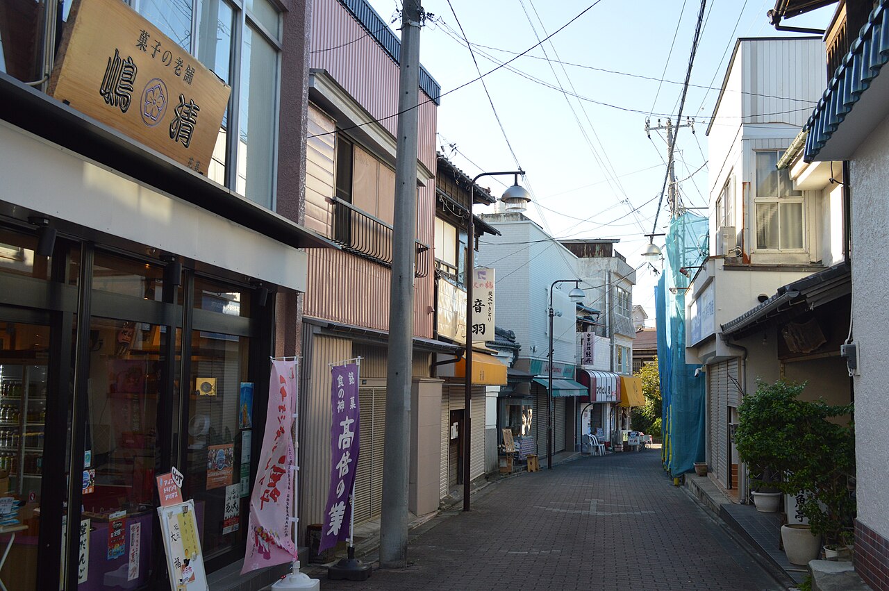A quiet narrow shopping street in Misaki lined with small shops, with banners and a utility pole on a sunny day