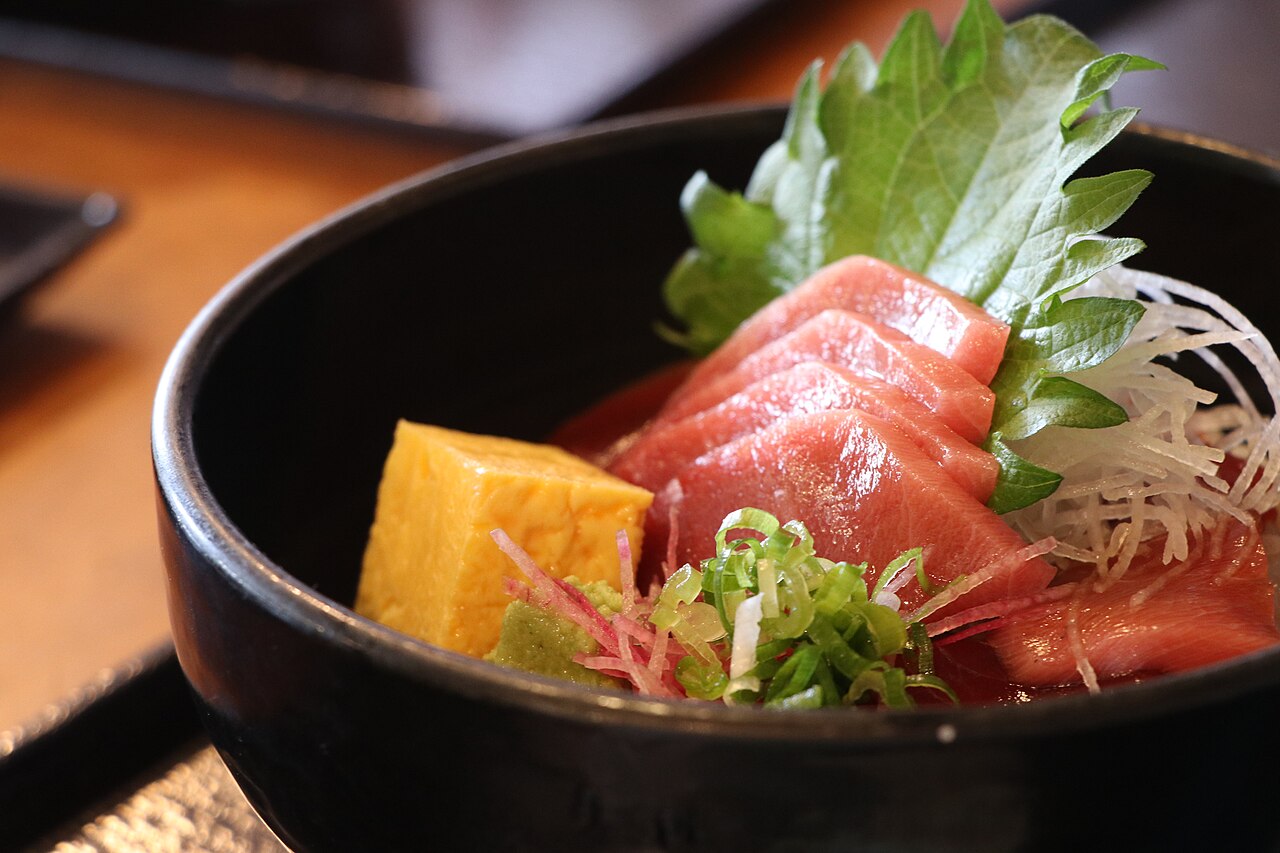 A black bowl of marinated tuna with a slice of fatty tuna, egg and shiso leaf and shredded garnish