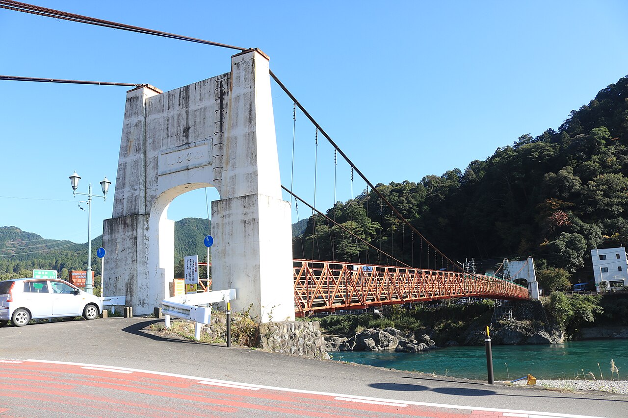Mino Bridge, an orange steel suspension bridge crossing the Nagara River, seen from its western pier.