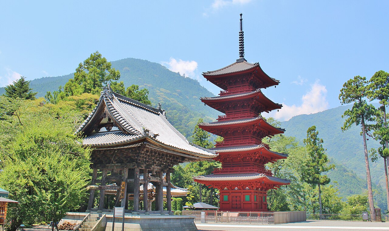 A five-story red pagoda and bell tower at Kuon-ji with green mountains behind