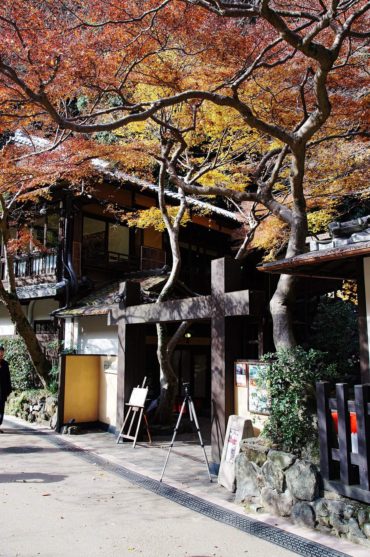 A traditional wooden building in Minoh Park framed by a canopy of orange and yellow autumn maple leaves.