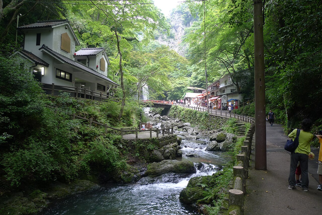 The Takimichi path along a mountain stream in Minoh, lined with traditional shops, with a red bridge leading toward the falls.