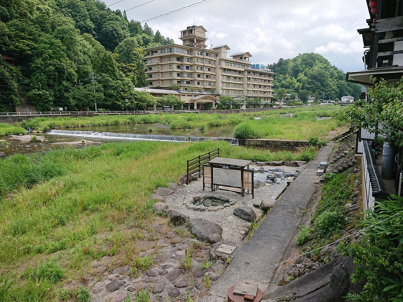A riverside open-air bath area by the Misasa river with a large hot-spring hotel on the far bank and green hills behind