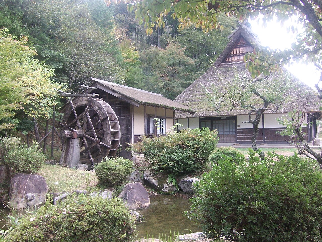 A water wheel and a thatched-roof building in the garden of the Miyama Kayabuki museum in autumn