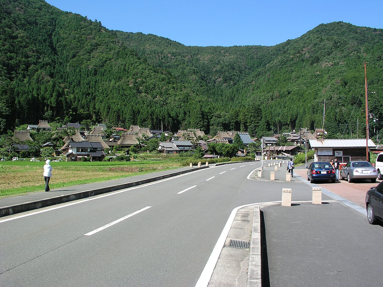 Thatched farmhouses in the Kita district of Miyama on a clear summer day, with forested hills behind and a road in front