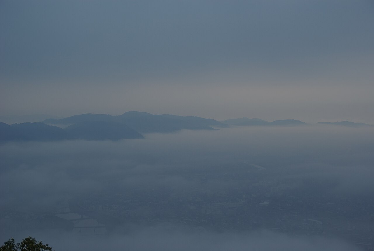 Pale morning mist lying over a wide basin, with low dark ridges rising out of the haze in the distance.