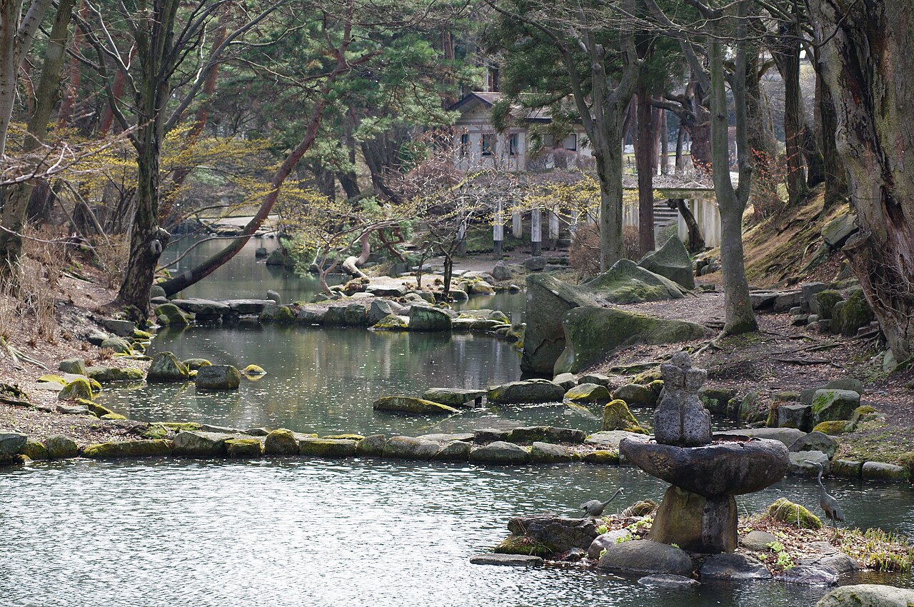 A pond with mossy stones, a small stone basin and pine trees in Iwate Park, the park around the Morioka Castle ruins.