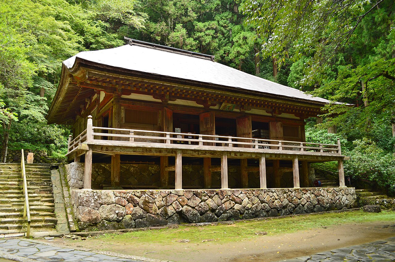 The wooden Kondo hall with a raised veranda on a stone-walled base, set against forested hillside.