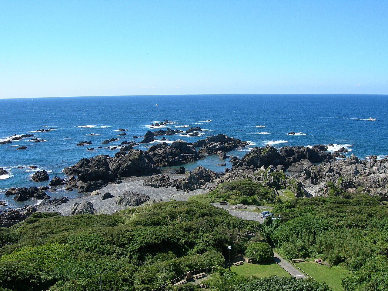Dark rocky reefs and tide pools along the shore of Cape Muroto seen from above, with white surf and the deep blue Pacific stretching to a straight horizon