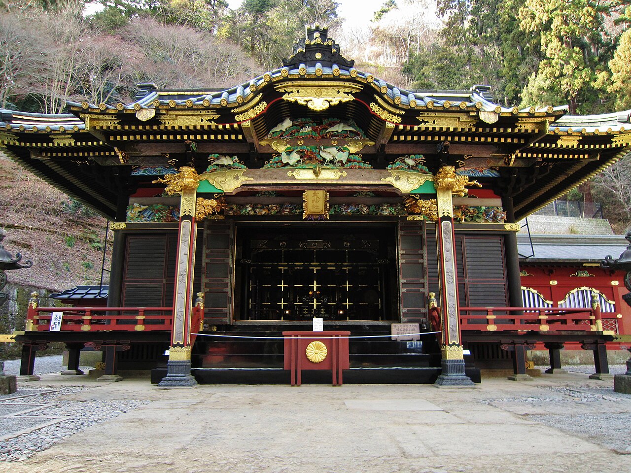 Three-part worship hall (haiden-heiden-honden) of Myogi Shrine seen from the stone approach, vermilion woodwork against a wooded hillside