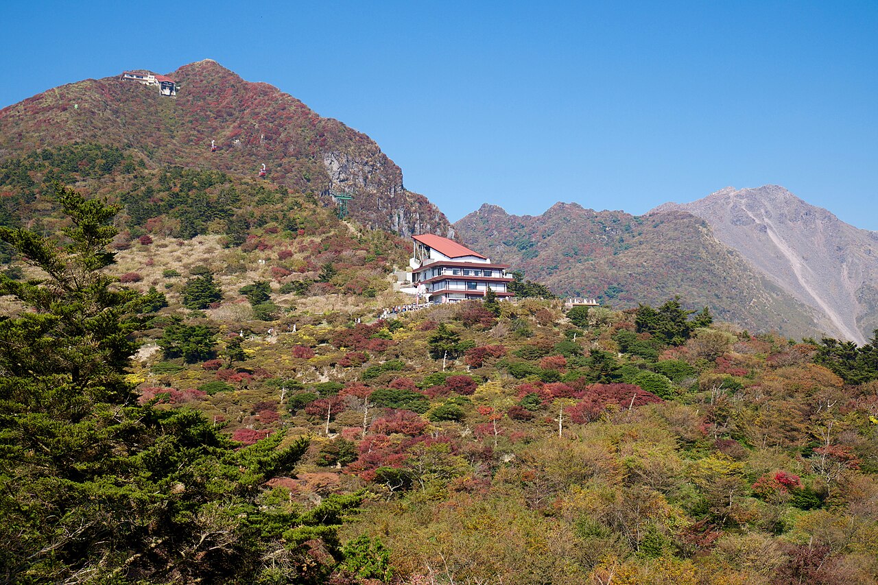 Autumn foliage on the Myokendake slope with the ropeway top station and Mount Fugen in the distance