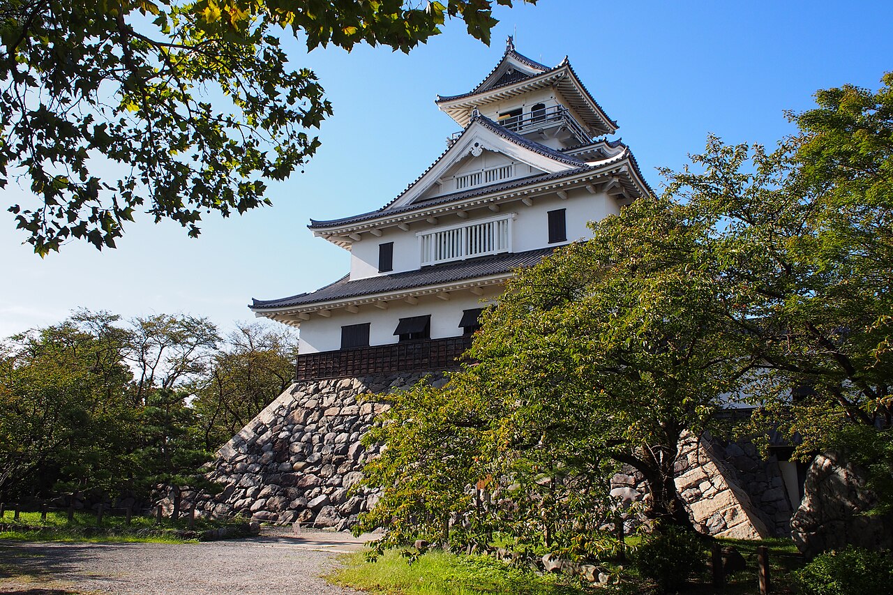 The white keep that houses the Nagahama Castle Historical Museum, rising above stone walls and green trees under a blue sky