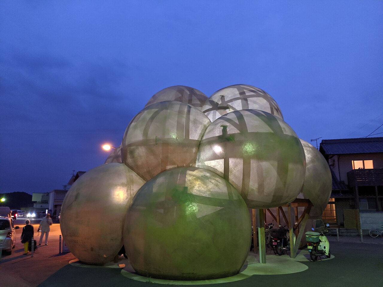 The round, mirror-like pods of the Honmura port terminal on Naoshima, with parked bicycles under its roof, seen at dusk