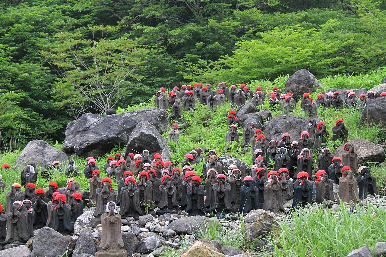 Rows of small stone Jizo statues wearing red caps among rocks and grass at Sessho-seki, Nasu