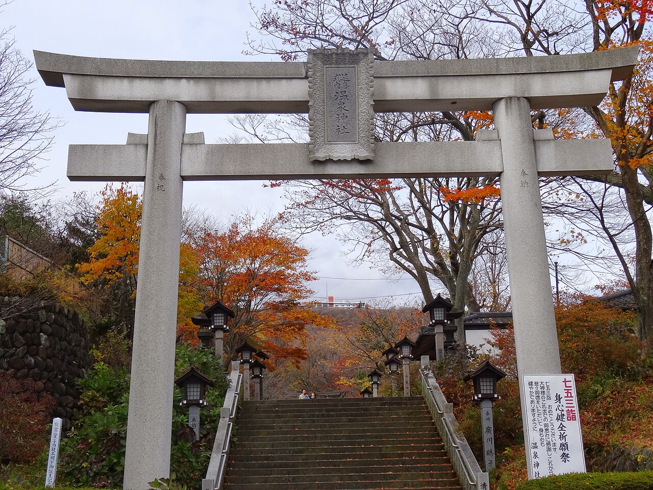 A stone torii gate at the top of a stone staircase lined with stone lanterns among autumn trees at Nasu Onsen Shrine