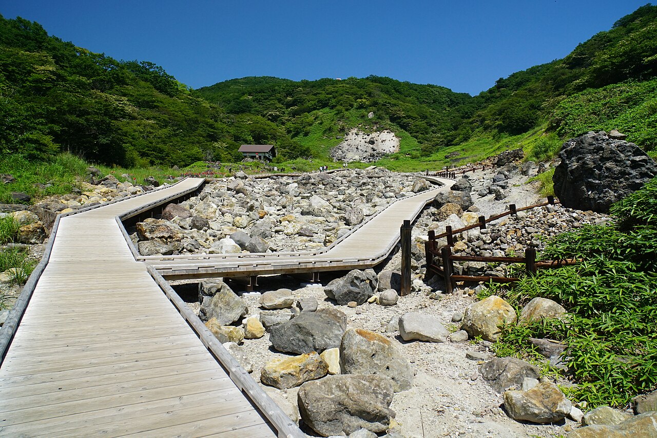 A boardwalk crossing the stony, barren Sessho-seki valley below a bare hillside in Nasu on a sunny summer day