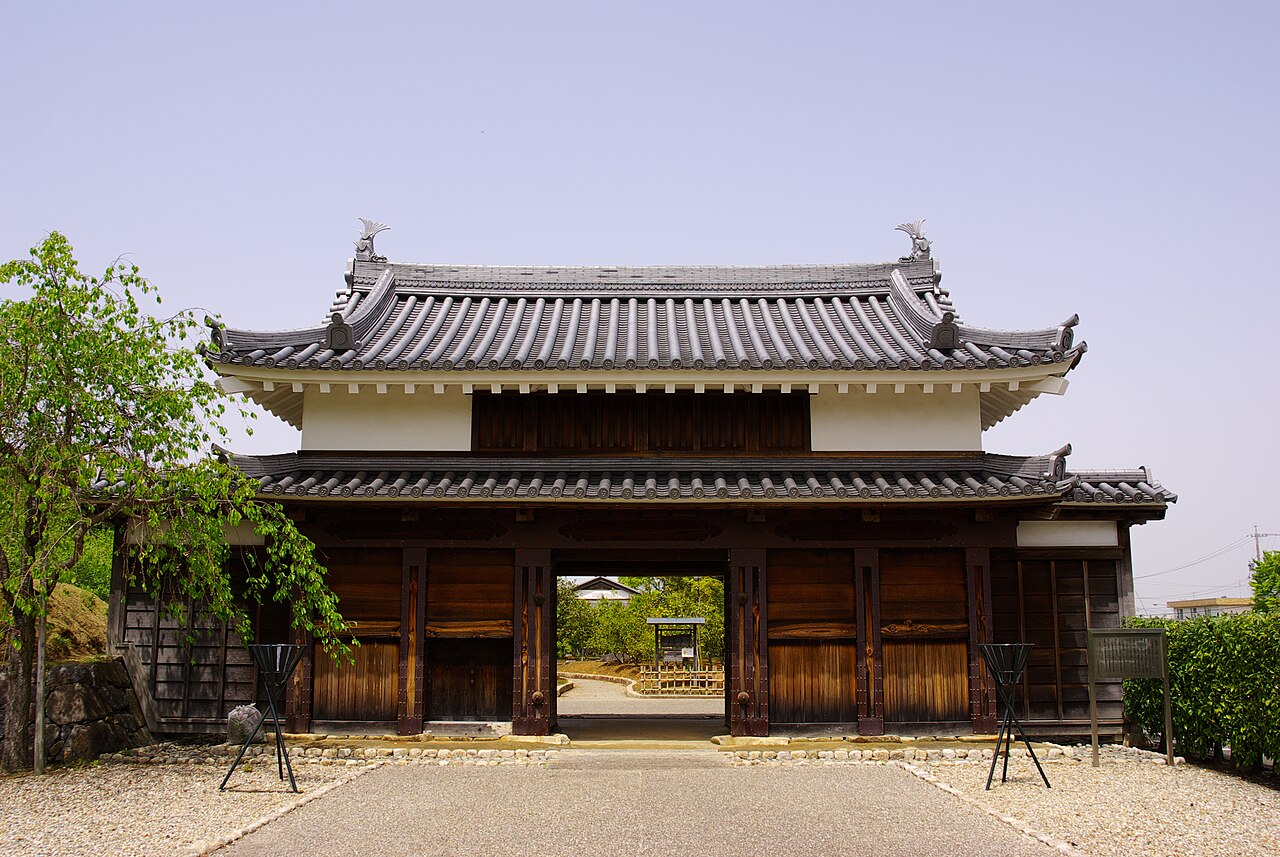 The tiled-roof Chuseki Gate of Nishio Castle with its wooden doors open onto a gravel path