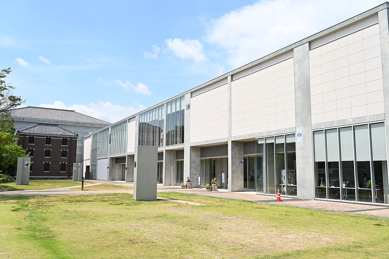 The modern white building of the Iwase Bunko library in Nishio beside a lawn, with an older red-brick storehouse behind it
