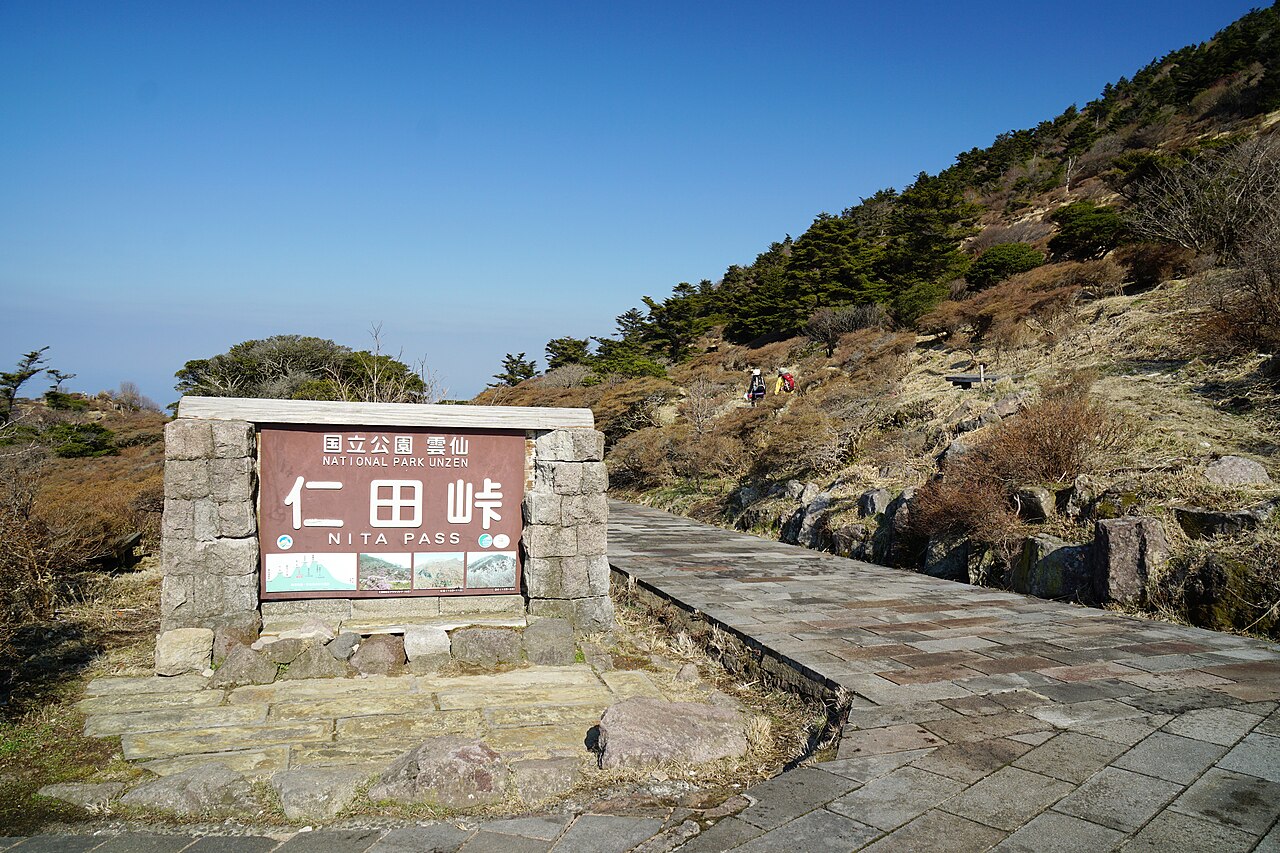 Stone Nita Pass signboard beside a paved path on the open, scrub-covered ridge
